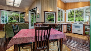 Un rincón comedor acogedor con una mesa y sillas de madera, una cocina con estufa, y ventanas amplias con vistas a zonas verdes.