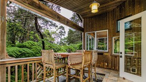 Una terraza de madera con una mesa y sillas, rodeada de exuberante follaje y vista a árboles.