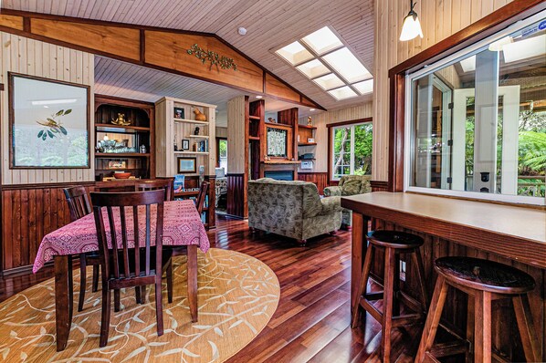 A cozy interior with a dining area, a fireplace, and a large window offering a view of greenery.
