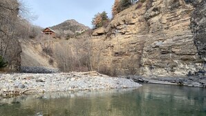 Une rivière aux eaux claires, bordée de rochers, avec une cabane en bois en arrière-plan.