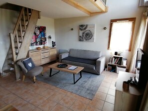 A living room with a sofa, a coffee table, a chair, a staircase, a bookshelf, and a window.