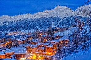 A snow-covered mountain village with traditional wooden buildings and a ski resort in the background.