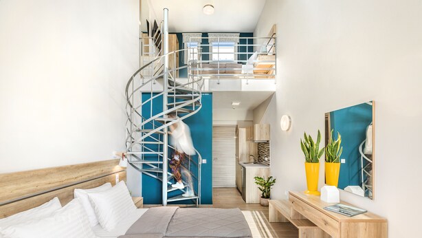 A modern bedroom with a spiral staircase, a bed, a desk, and a view of the kitchen. - Sunshine Apartments (Dio-Olympos)