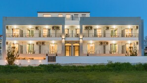 A modern two-story building with balconies, large windows, and outdoor seating areas. - Sunshine Apartments (Dio-Olympos)