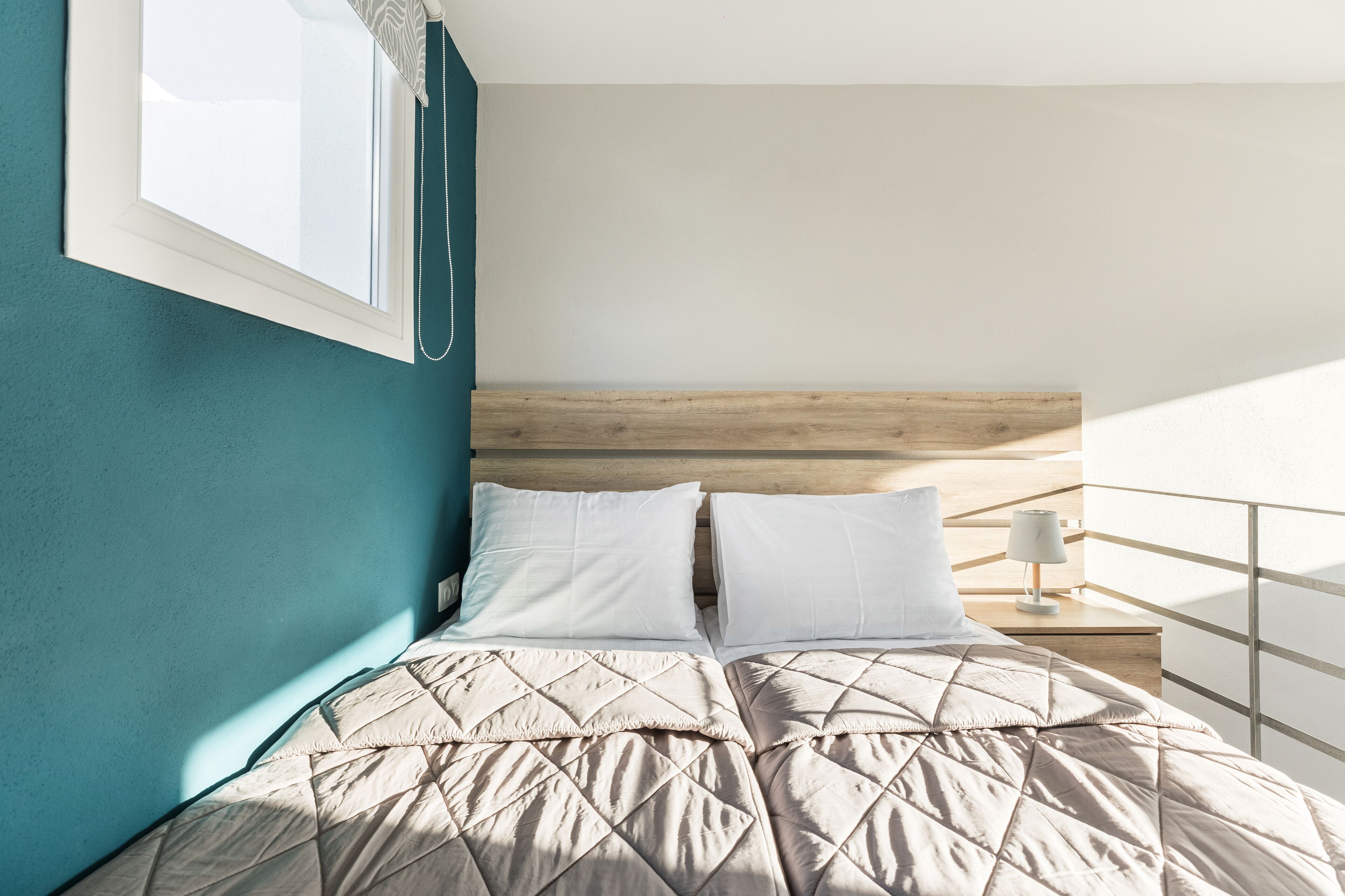 Un dormitorio con una cama, una mesita de noche, una lámpara y una ventana.