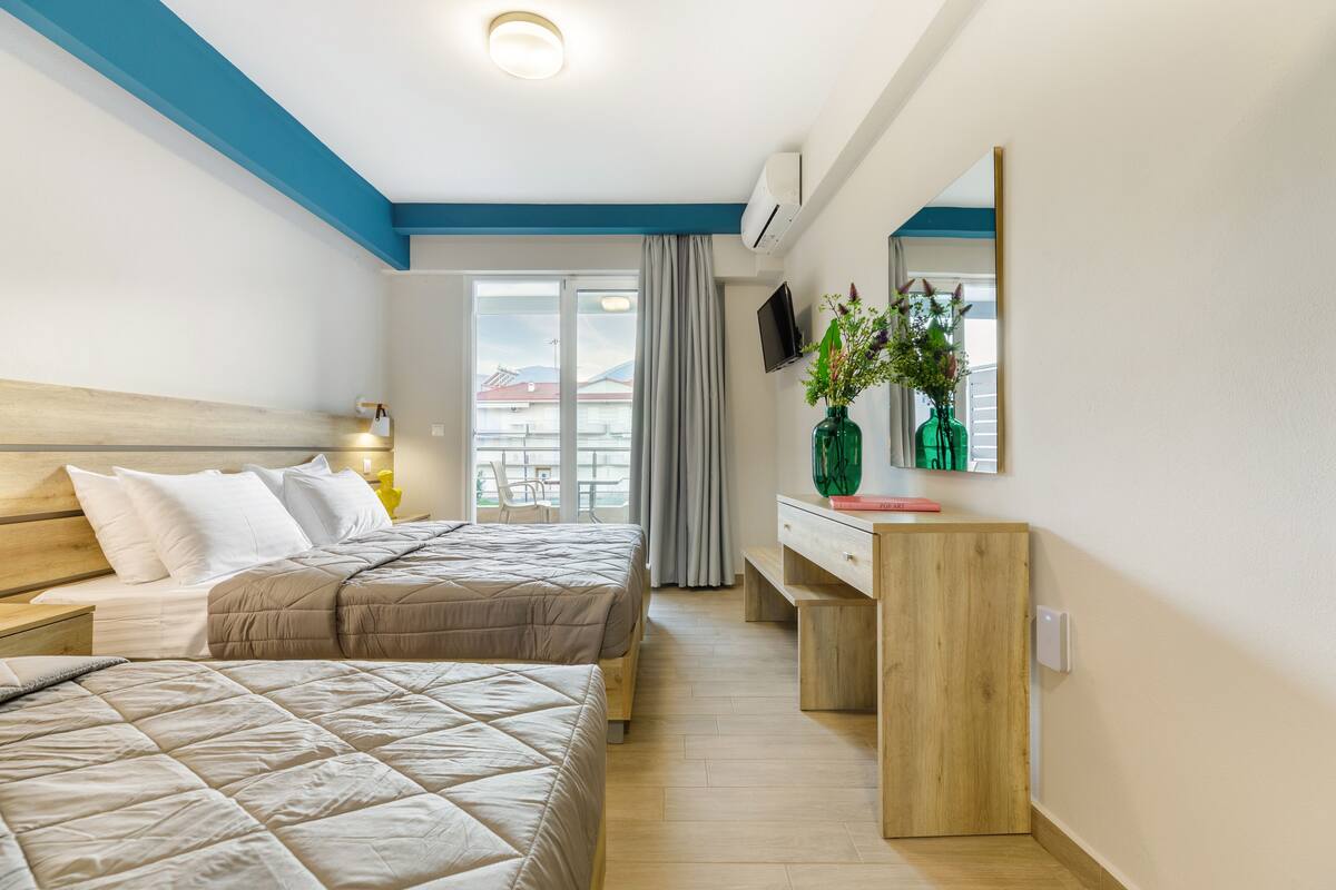 A hotel room with two beds, a wooden dresser, a TV, and a large window with a view of buildings.
