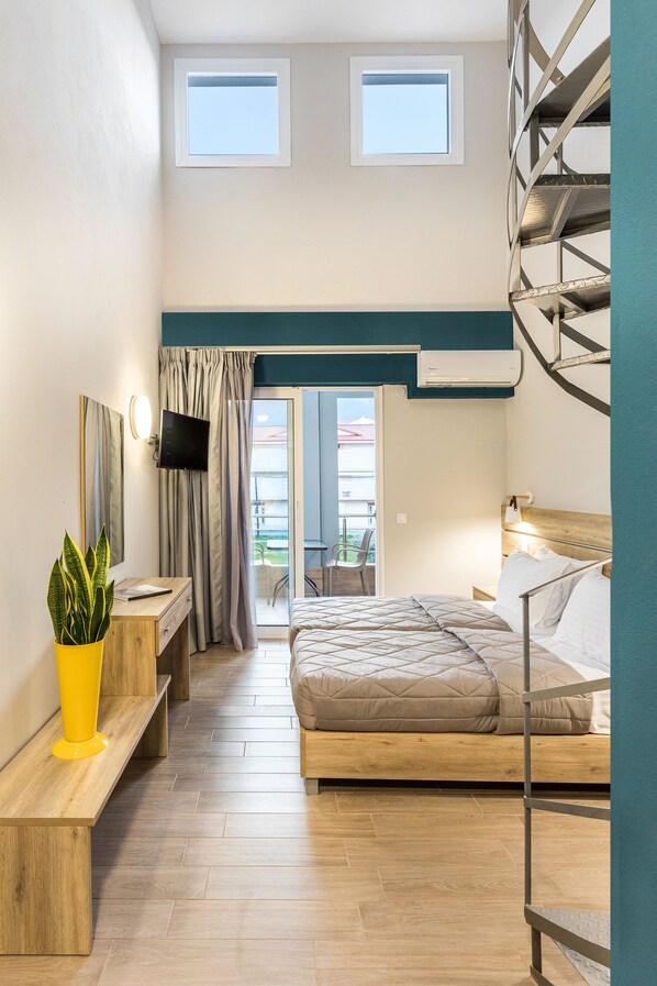 Habitación de hotel compacta con literas, un escritorio con silla, una pequeña planta en maceta y un televisor montado en la pared.