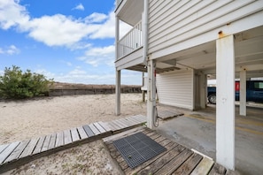 A beachfront property with a covered outdoor area, a wooden deck, and a vehicle in the background.