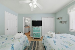 Une chambre avec deux lits, une télévision, une commode et un ventilateur de plafond.