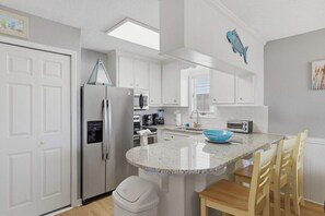 A modern kitchen with white cabinetry, a stainless steel refrigerator, a built-in oven, a microwave, a coffee maker, and a toaster.