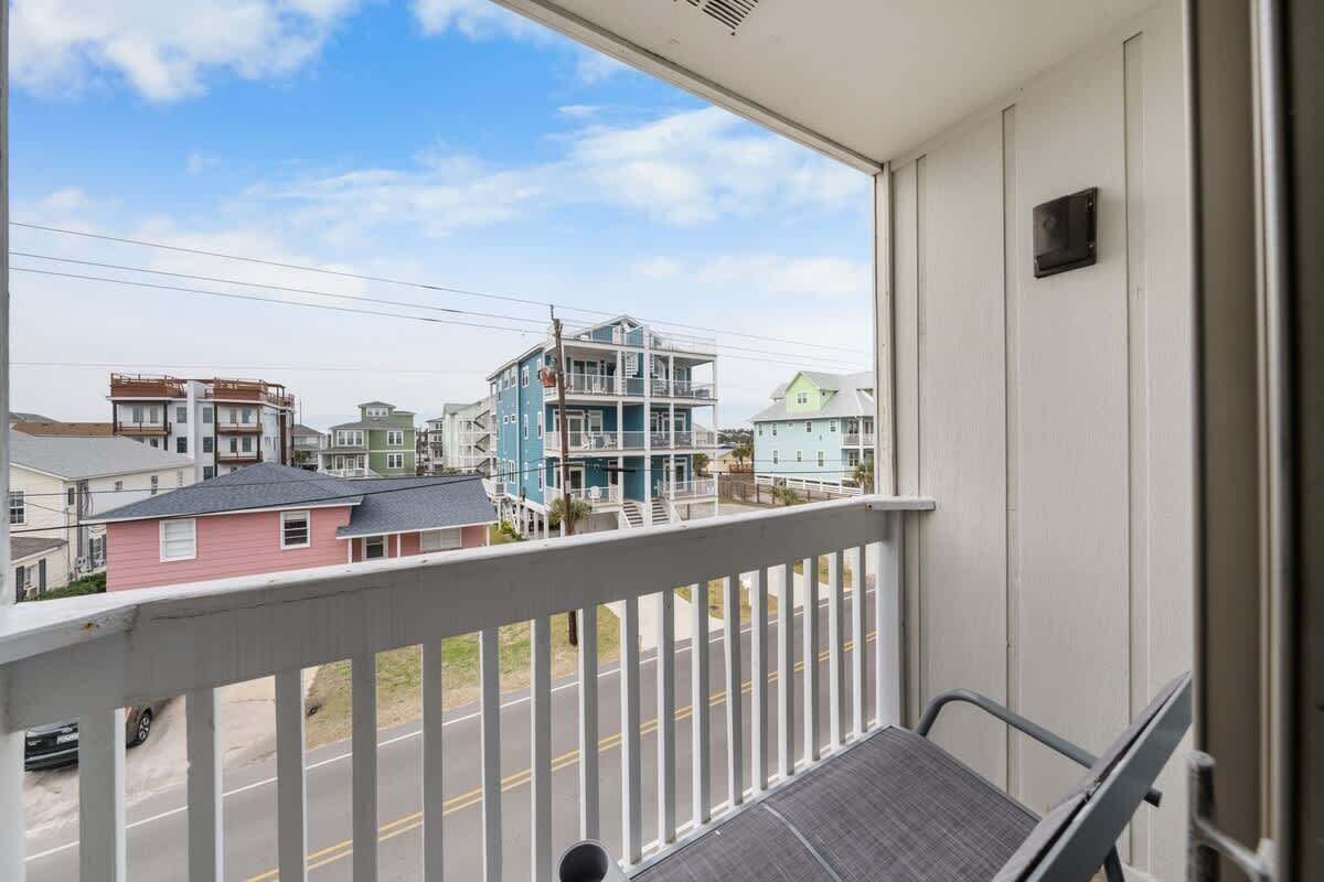 A balcony with a view of multi-story buildings, a street, and a clear sky.