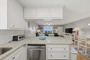 A modern kitchen with white cabinetry, a built-in dishwasher, a toaster, and a view of the ocean through the window.