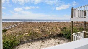 Vista sulla spiaggia da un balcone con ringhiera in legno, spiaggia sabbiosa e oceano.