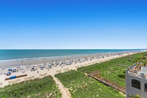A beach with a wooden walkway leading to a building with a balcony.
