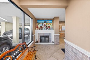 A hotel lobby with a fireplace, a bench, and a view of parked cars outside.