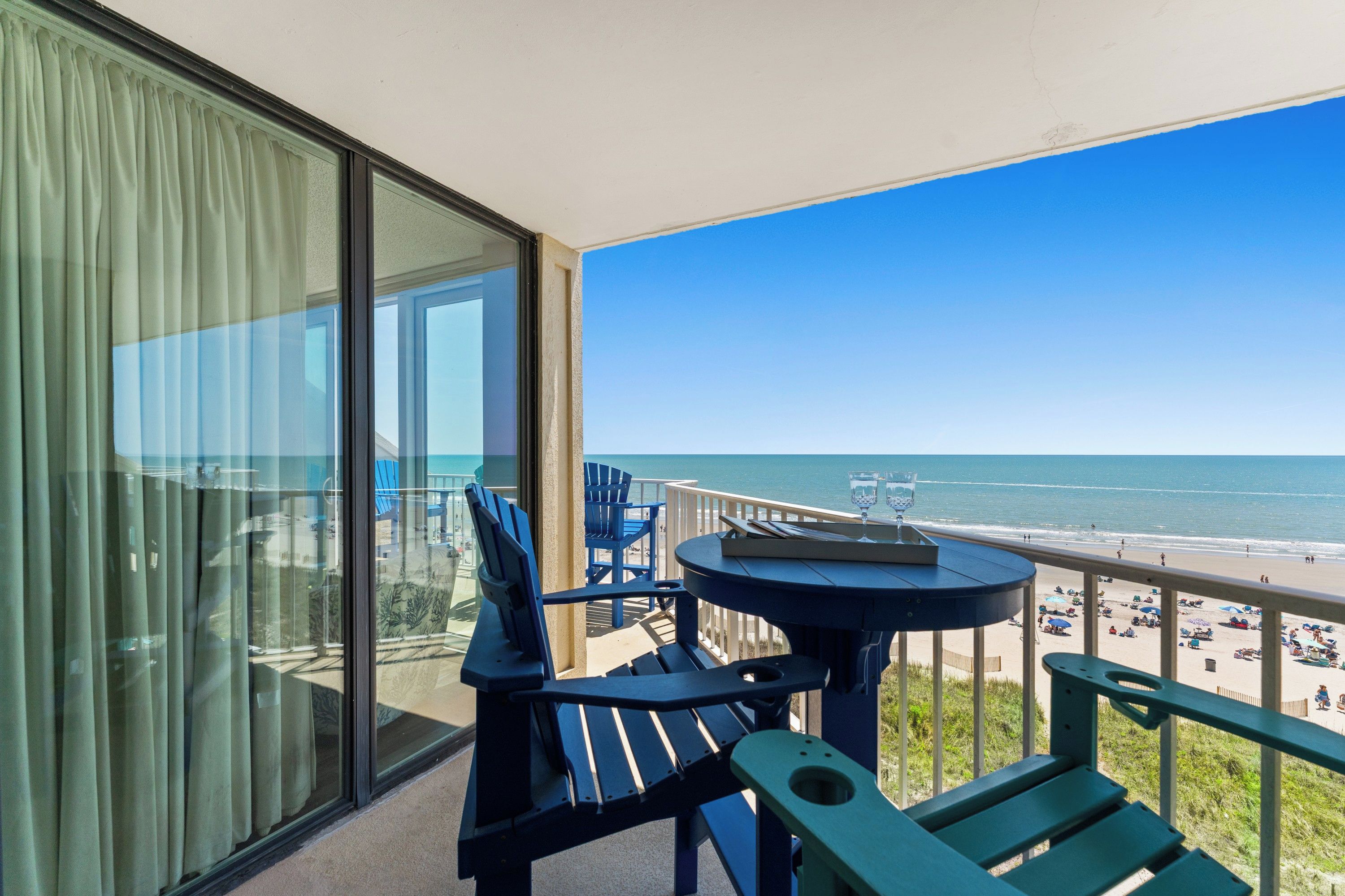 A balcony with a view of the beach, featuring a table and chairs.