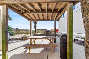 An outdoor wooden pergola with a picnic table and a trash can.