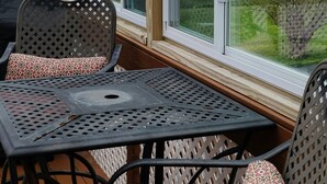 Una sala de estar con ventanales que dan a un lago, con una mesa y dos sillas con cojines estampados.