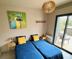 Ein Schlafzimmer mit einem großen Bett, zwei Nachttischen, einer Lampe, einem Papageienbild und Blick auf eine Terrasse.