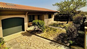 A house with a tiled roof, a garage, and a paved courtyard with a small tree and shrubbery. - Modernes Ferienhaus in Erster Reihe Gegenüber der Dünen (Hourtin)