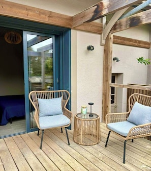 Una terraza de madera con dos sillas de mimbre y una mesa redonda pequeña con una vela.