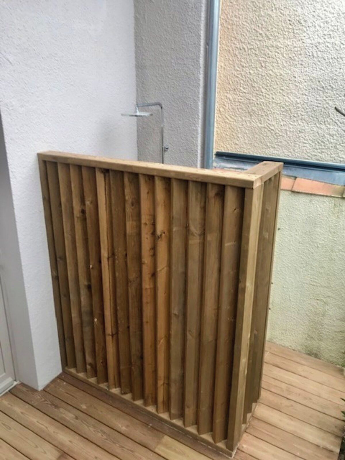 Ett staket av trä med vertikala ribbor, ett trädäck och en vägg med en strukturerad yta.