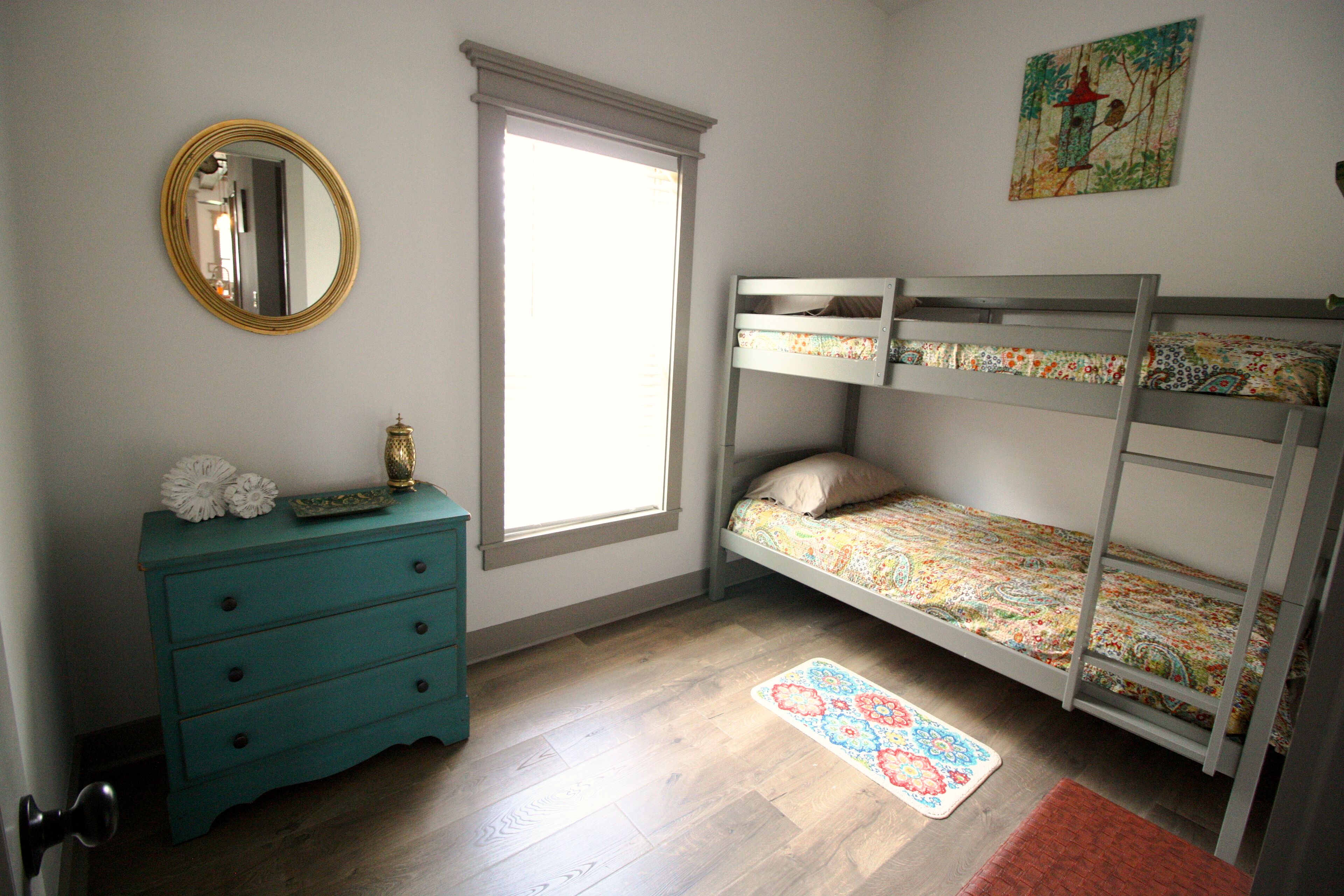 Une chambre avec un lit superposé, une commode, un miroir et une fenêtre.
