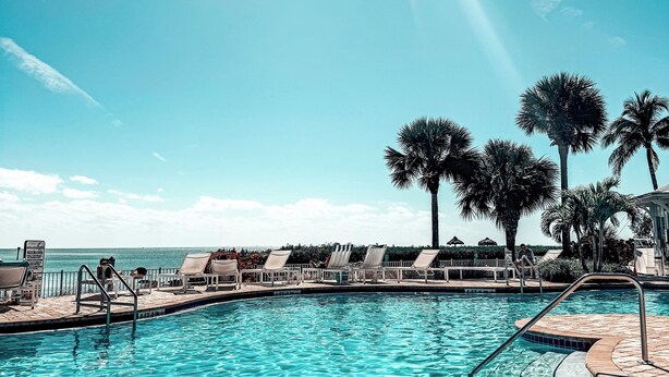 A clear blue pool with sun rays, palm trees, and lounge chairs. - Oceanside Getaway: Beautiful Home with Boat Slip, Pool & Beach - Gated community (Islamorada)