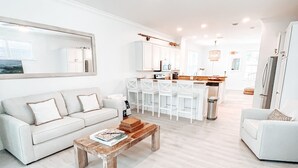 A spacious living room with a white sofa, a coffee table, and a dining area with white chairs. - Oceanside Getaway: Beautiful Home with Boat Slip, Pool & Beach - Gated community (Islamorada)