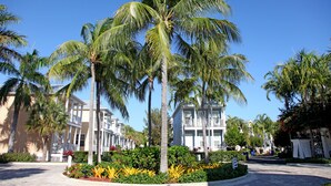 A resort with palm trees, a paved walkway, and a building with balconies. - Oceanside Getaway: Beautiful Home with Boat Slip, Pool & Beach - Gated community (Islamorada)