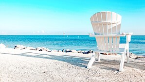 A white beach chair on a sandy beach with a clear blue sea and a distant lighthouse. - Oceanside Getaway: Beautiful Home with Boat Slip, Pool & Beach - Gated community (Islamorada)