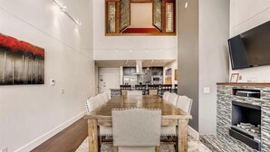 A modern dining area with a long wooden table, white upholstered chairs, and a fireplace with a stone surround. - Huge condo in Keystone, sleeps 14, great location (Dillon)