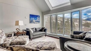 A modern living room with a large window offering a mountain view, a grey sofa, patterned cushions, and a side table with a lamp. - Huge condo in Keystone, sleeps 14, great location (Dillon)