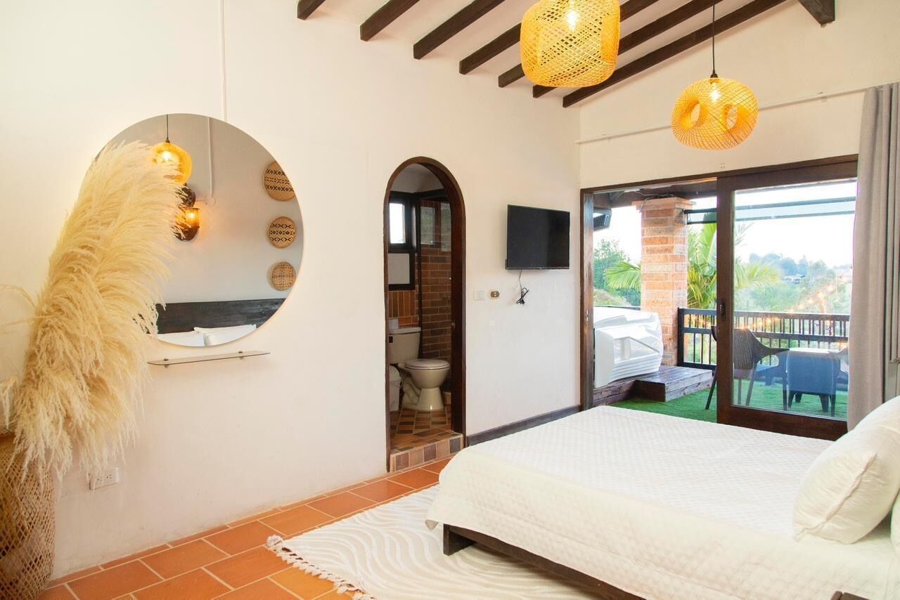 Quarto com cama, espelho, televisão e varanda com vista.