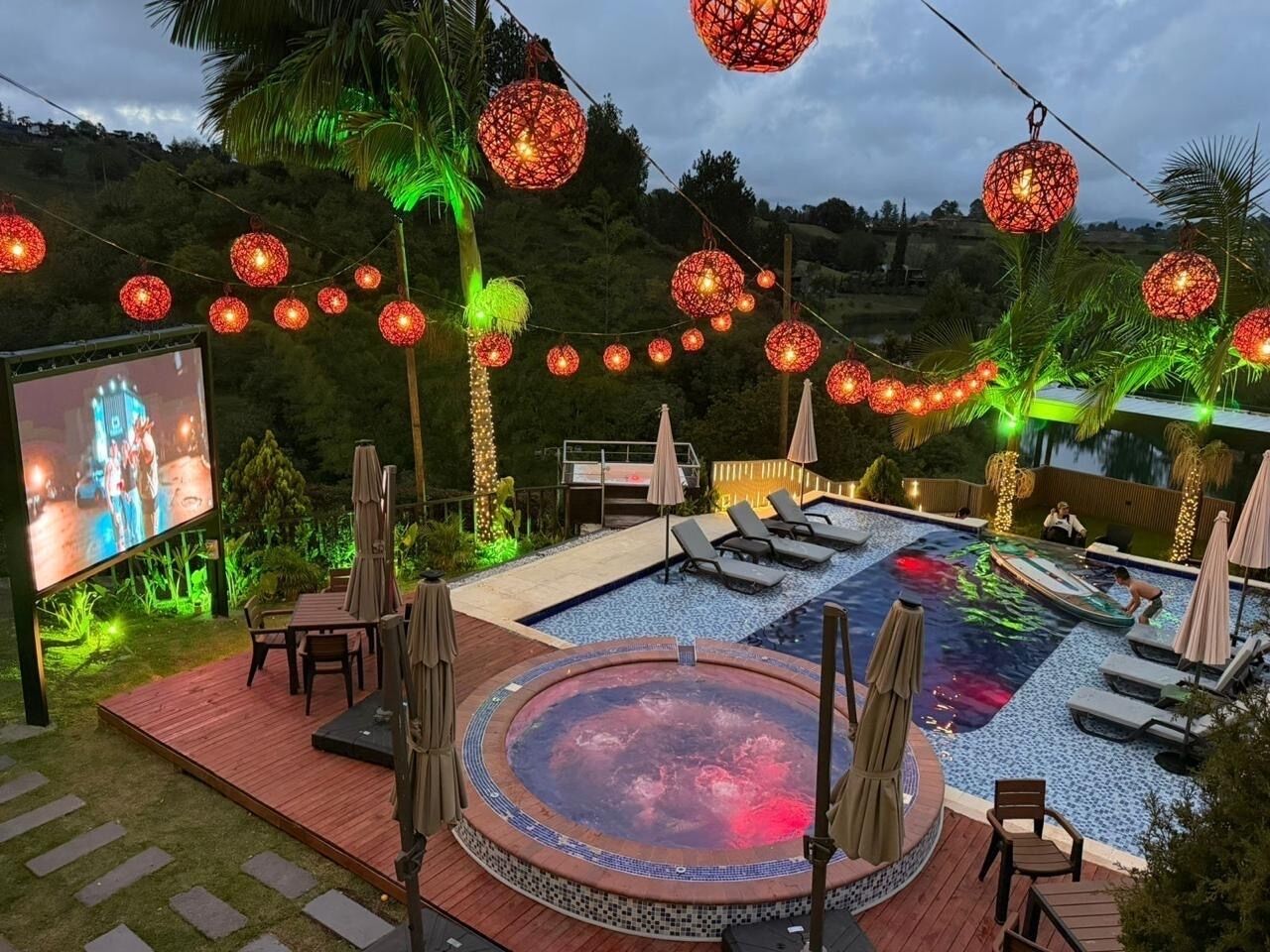 Uma área de piscina com espreguiçadeiras, uma banheira de hidromassagem e luzes decorativas.