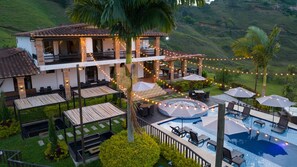 Una casa de dos pisos con piscina, mobiliario exterior e iluminación colgante.