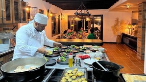 Un chef prépare des plats dans une cuisine bien éclairée, avec en arrière-plan une vue sur les clients qui dînent.