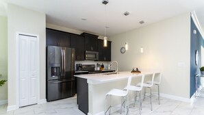 A modern kitchen with dark cabinets, stainless steel appliances, a white island with bar stools, and pendant lighting.