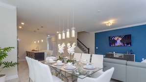 A modern dining area with a glass table, white chairs, and a chandelier.