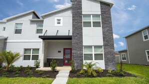 A modern two-story house with a stone facade, a red door, and a small front porch.