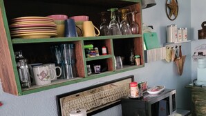 A kitchen with a microwave, a table with a blue patterned cloth, and various kitchen utensils and dishes on shelves.