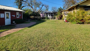A residential area with a well-maintained lawn, a pathway leading to a gated entrance, and two houses with visible signage.