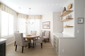 A modern kitchen with a dining area, featuring a round wooden table, four upholstered chairs, a chandelier, and built-in shelves with decorative items. - Gorgeous Lake Front Home, Central Location (Tualatin)
