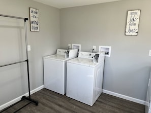 A laundry room with two front-loading washers and dryers, a drying rack, and two wall-mounted signs. - Walk Everywhere | Lake, Strip & Wineries (Geneva)