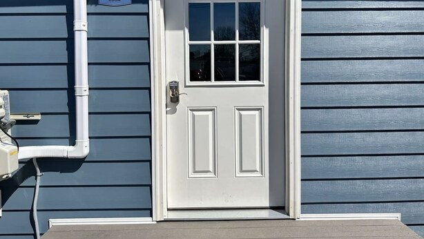 Una puerta blanca con una ventana, un cartel que indica lavandería y una pared exterior blanca.