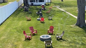 Un espacio al aire libre con césped, varias sillas Adirondack y un hogar circular para fuego.