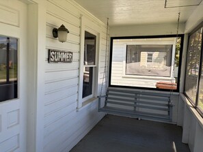 A porch with a swing, a 'SUMMER' sign, and a window overlooking a yard.