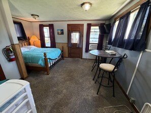 A compact room with a bed, a small table with chairs, a television, and a door.
