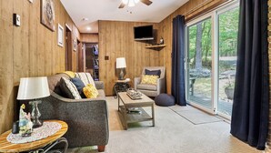 A cozy living room with a ceiling fan, a TV, and a large window with curtains.