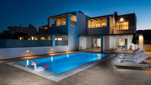 A modern pool area with a clear blue pool, lounge chairs, and a decorative unicorn float. - South Beach Villas - 2 bedroom sea view with heated pool (Γεννάδι)